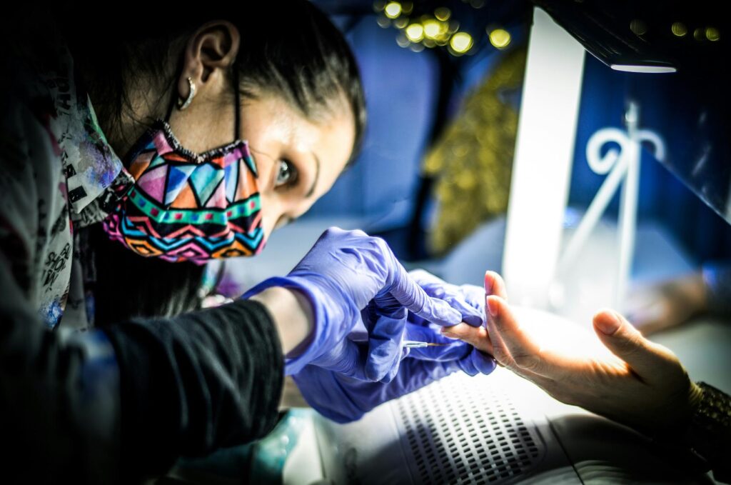 Woman applying gel polish to her nails under a UV lamp one of the commun Gel Manicure Tips.