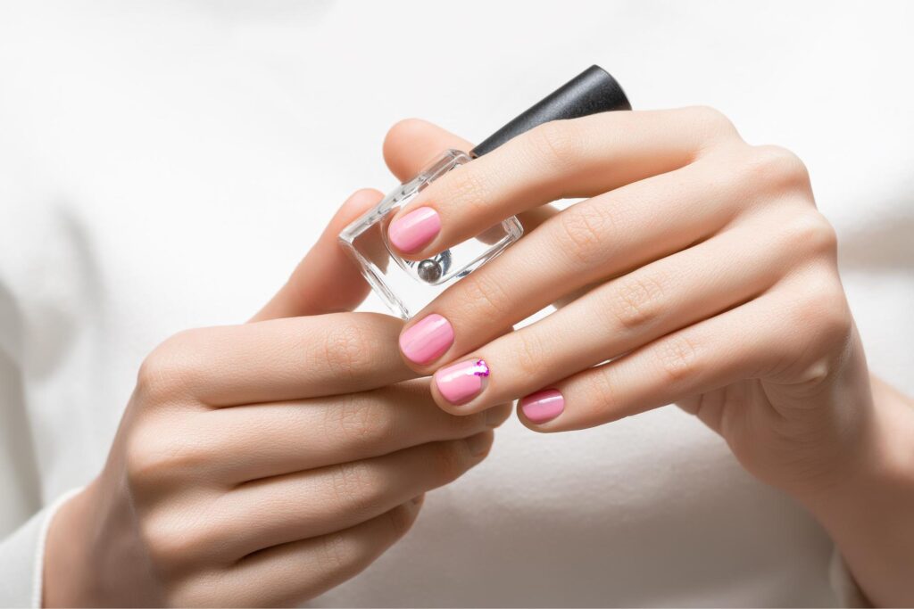 a hand holding a top coat with pink nails